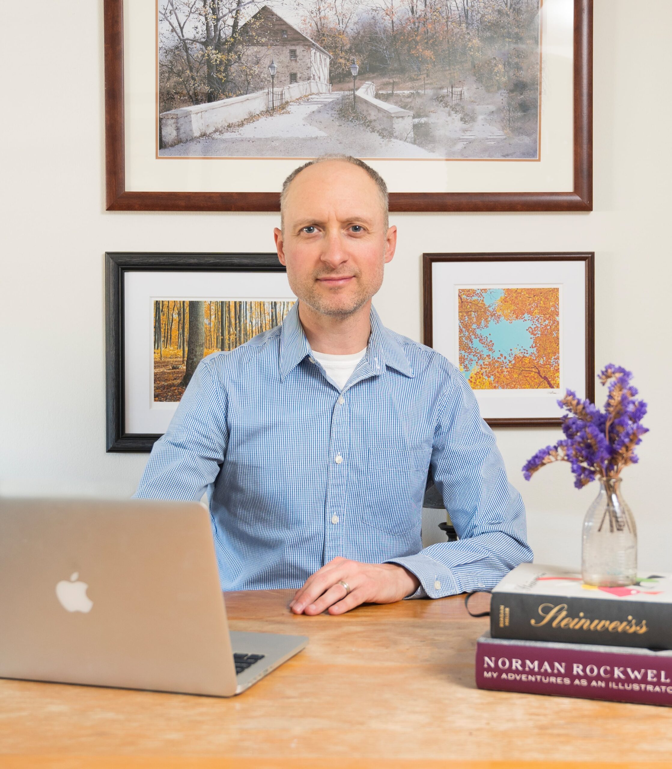 Portrait of Craig Schlanser working on a laptop, and seated in front of paintings