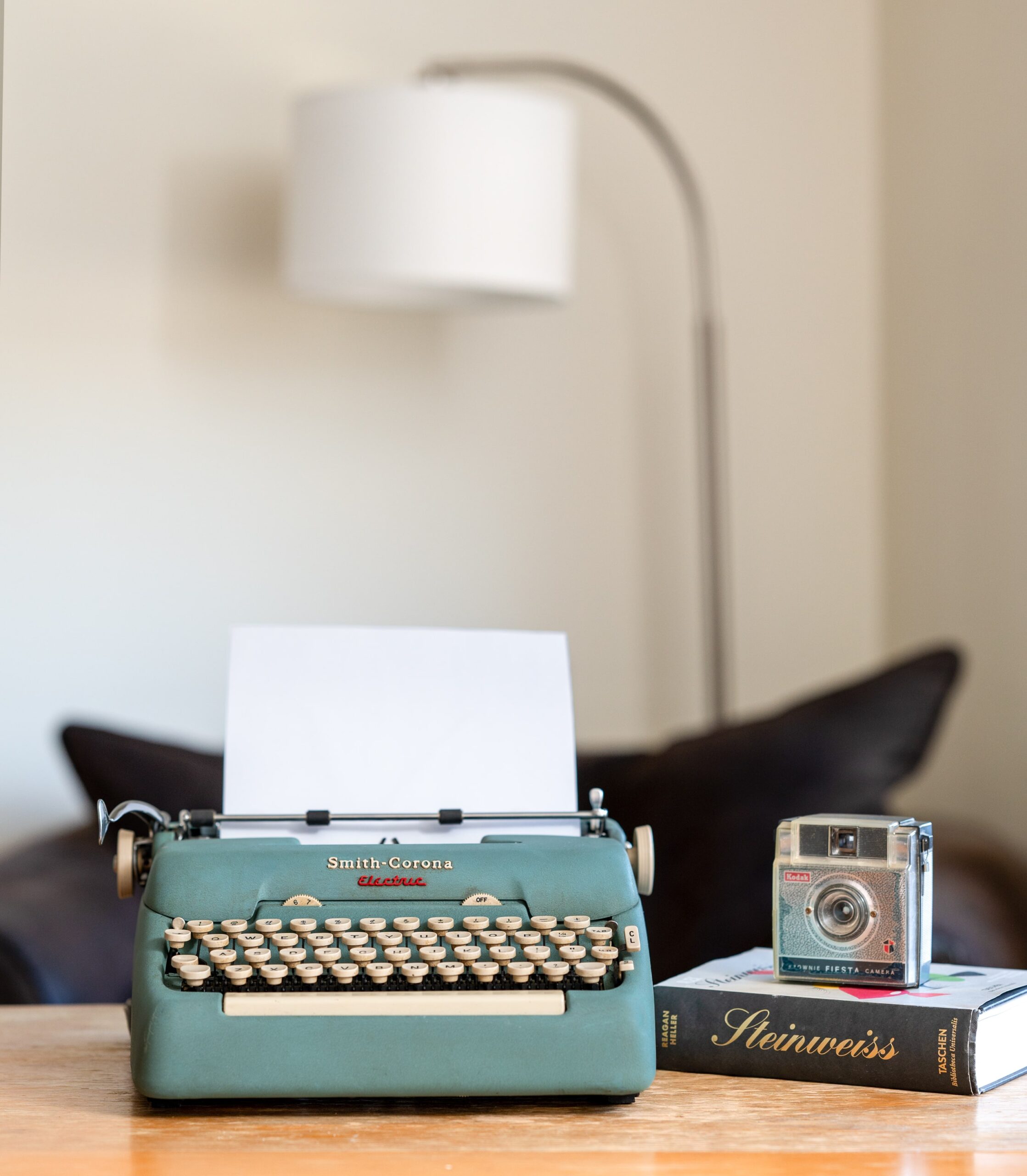 Typewriter and camera on a desk with a modern lamp in the background